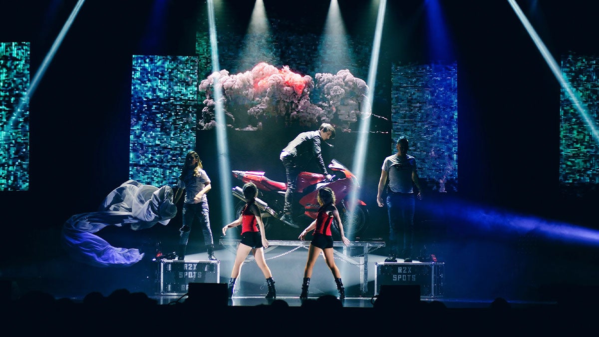 Reza on stage with motorcycle and performers at Reza Edge of Illusion Show